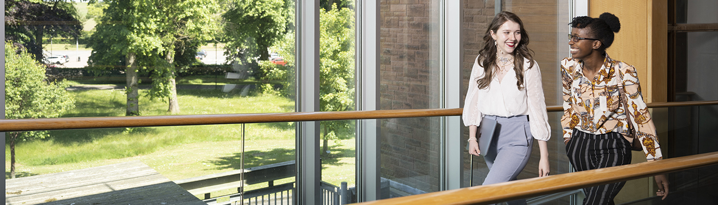 Students at Dumfries Campus walking past window with trees outside