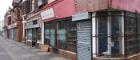 Row of shops in an inner city area. Many are boarded up and in disrepair. This is Moss Side, Manchester, UK.