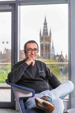 A student sitting in a chair with the University of Glasgow in the background.