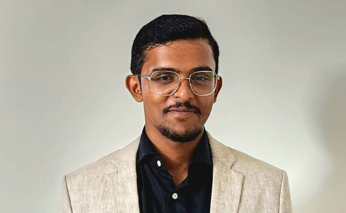 A man in a light coloured linen blazer in front of a plain blackground