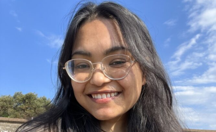 A woman smiles at the camera in front of a blue sky background