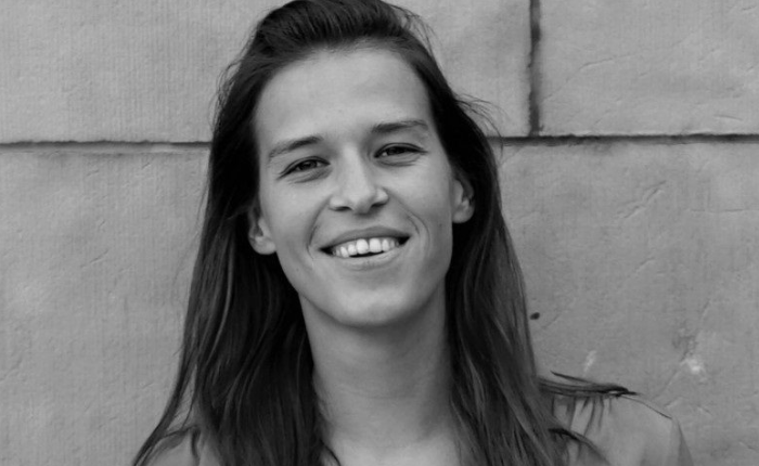 A black and white photo of a woman smiling in front of a brick wall