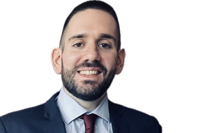 A man in a smart suit smiles before a plain white background