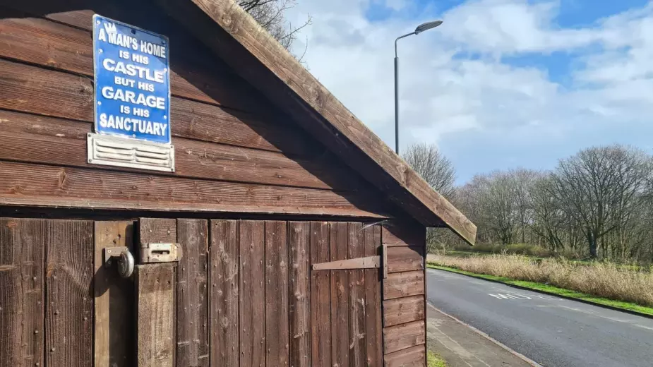 Blue sign reading 'A man's home is his castle but his garage is his sanctuary' on brown wooden shed