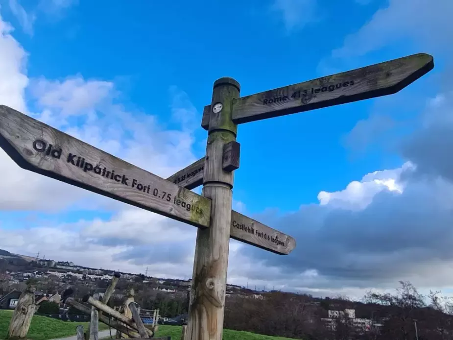 Wooden signpost reading, from top to bottom, 'Rome 413 leagues', 'Old Kilpatrick Fort 0.75 leagues', 'Castlehill Fort 0.6 leagues'