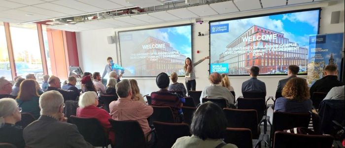 Photo of a group of staff attending a community engagement event in May 2023, with two colleagues presenting slides