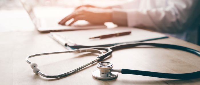 Photo of health care professional working at laptop with stethoscope