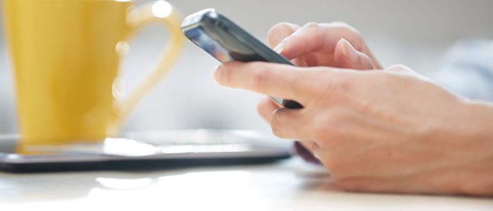 Photo of person's hand holding a mobile with yellow mug beside them