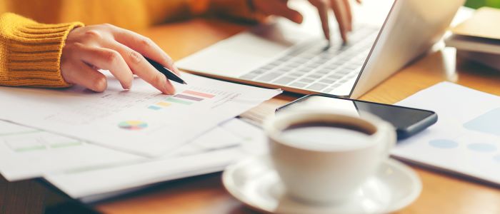 Photo of person working on laptop with charts and coffee cup