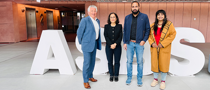 Prof Robert Paton and guests standing for a photo in front of giant 'ASBS' letters, in the Atrium of the Adam Smith Business School