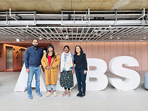 Group photo of University of Glasgow academics with guests from IIM Indore, standing in front of giant 'ASBS' letters in the atrium of the Adam Smith Business School