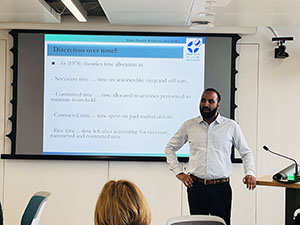 Academic presenting standing in front of a PowerPoint slide screen