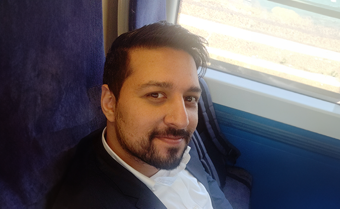 A person wearing a blue suit sitting on a train taking a selfie beside a window