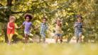 A group of boys and girls running across grass on a sunny day.