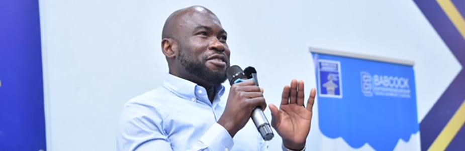 Iyke Ikegwuonu standing on stage presenting at a conference, holding a microphone