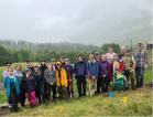 A group of people smiling at the camera wearing wet weather gear. The sky is very grey and there are hills in the background.