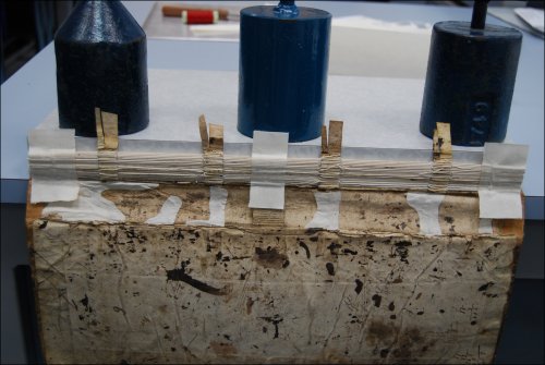 This photograph shows the textblock being attached to the cover of the logbook with parchment sewing support strips during conservation treatment.  (GUAS Ref: UGC 182. Copyright reserved.) 