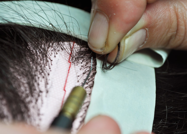 Hairs on a wig being knotted by hand