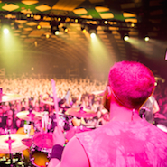 A photograph of a band in front of a large crowd, taken from behind the drummer.