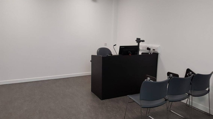 Flat floored teaching room with rows of tablet chairs, visualiser, and PC