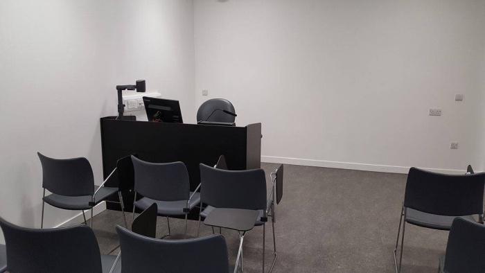 Flat floored teaching room with rows of tablet chairs, visualiser, and PC