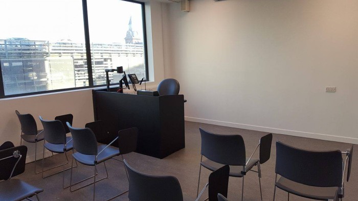 Flat floored teaching room with rows of tablet chairs, visualiser, and PC