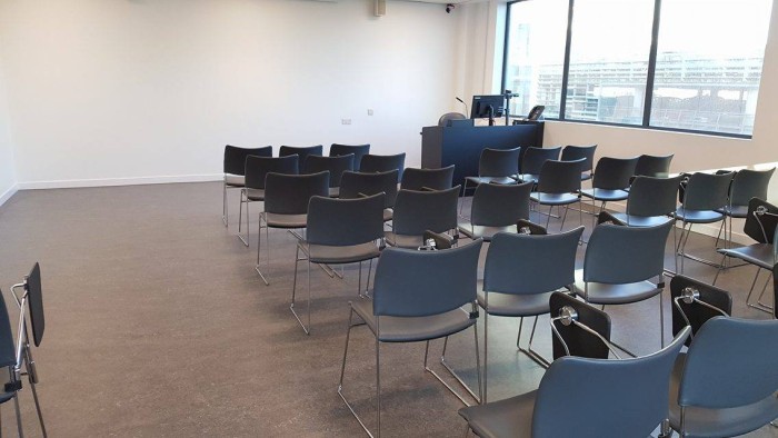 Flat floored teaching room with rows of tablet chairs, visualiser, and PC