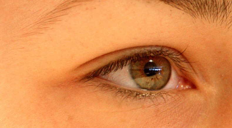 close-up photo of a green/brown eye framed by parts of a white face with brown lashes and brows