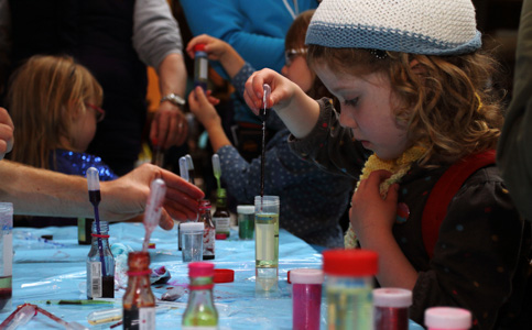 Photograph showing a child dropping a pipette of coloured liquid into a test tube. 