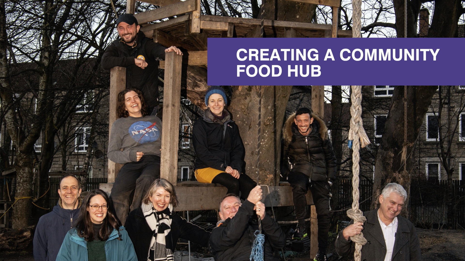 A group of people posing around a tree and swing at Baltic Street Adventure Playground in Glasgow