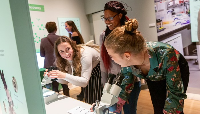 Three participants look through microscopes at theParasites_ Battle for Survival, an immersive exhibition held at the National Museum of Scotland (NMS)