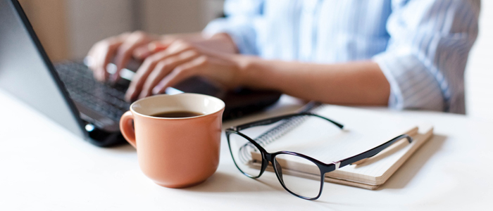 person on laptop with glasses coffee and notepad