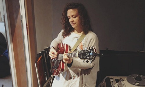 Woman playing guitar in a darkened room near a light window