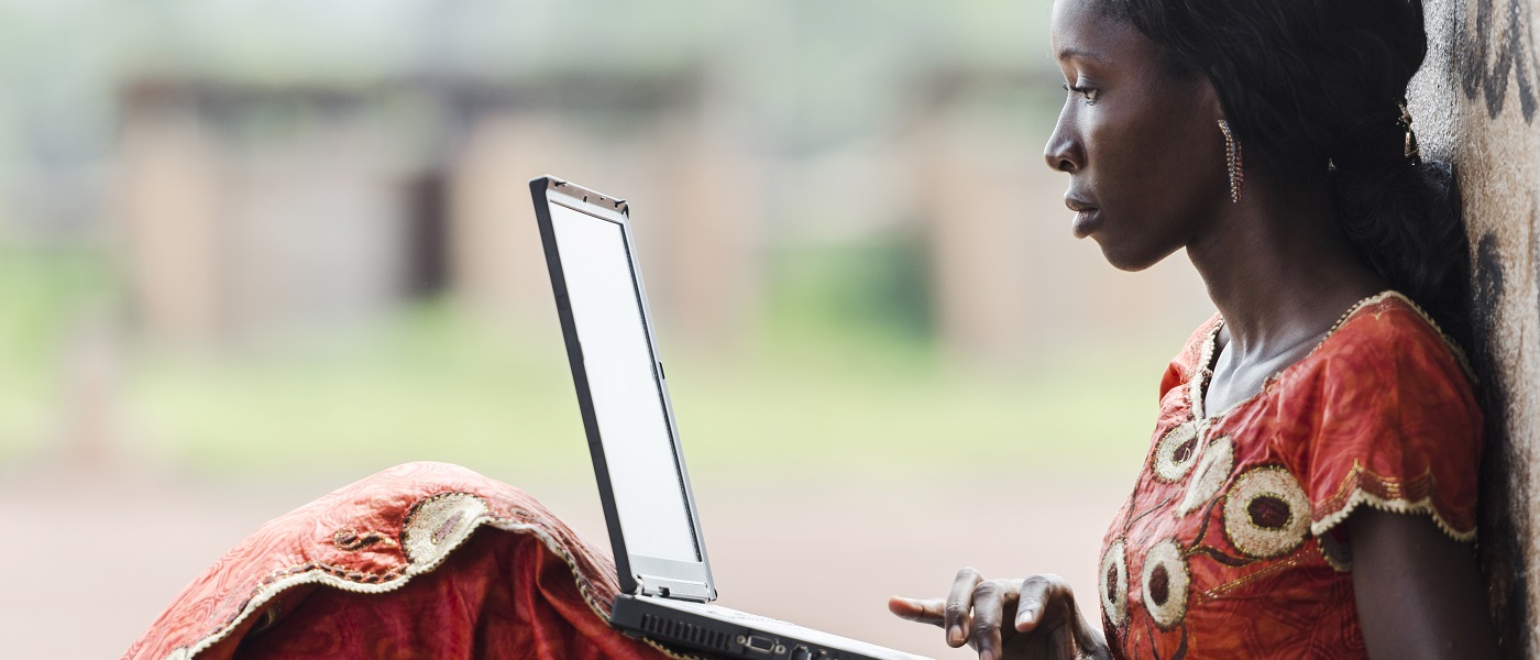 A young African woman sitting and leaning against a wall to use her laptop.Image credit: borgogniels | iStockphoto https://www.istockphoto.com/photo/technology-symbol-african-woman-studying-learning-lesson-gm529835071-54284780