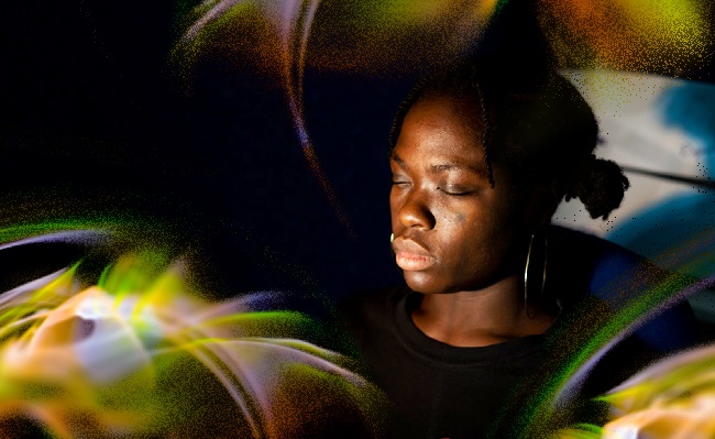 An image of a woman sitting with her eyes closed surrounded by rainbow shafts of light. Image Credit Brenna Duncan 