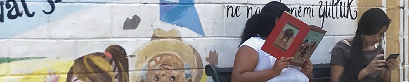 two women reading books on a bench infront of a colourful mural