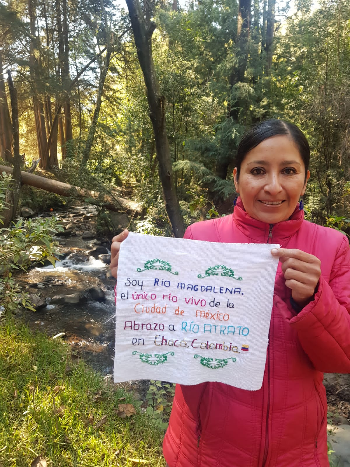 Women holding crotched message on fabric next to river