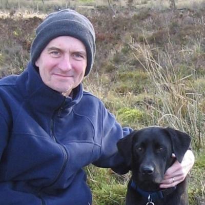 A man sitting with a black dog in a field