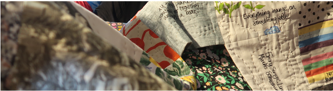 A multicoloured quilt with writing embroidered on it.