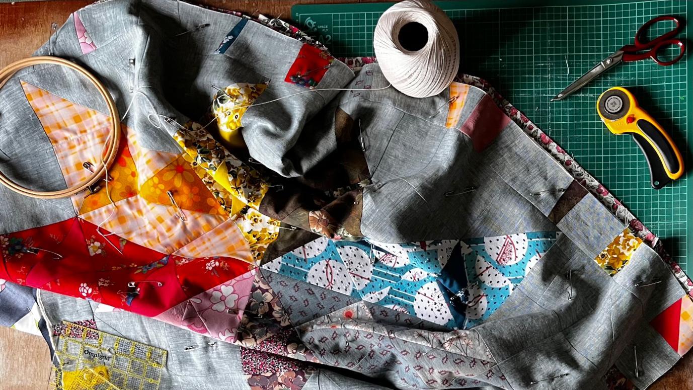 Pieces of quilting lay on a table with sewing tools laid around them.