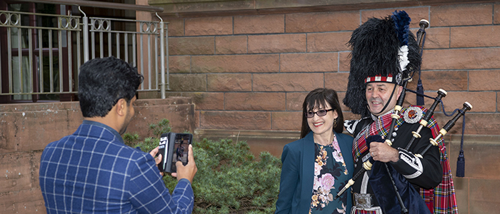 Student taking a photo of friend beside a bag piper