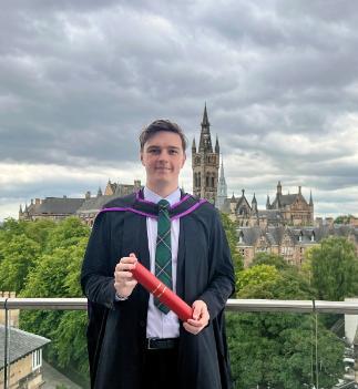 Young male wearing graduation gown standing in front of University Main Building 