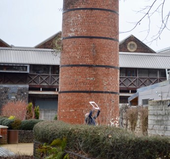 a photo of an individual looking at the sky through a large white frame, in the background is a brick smokestack