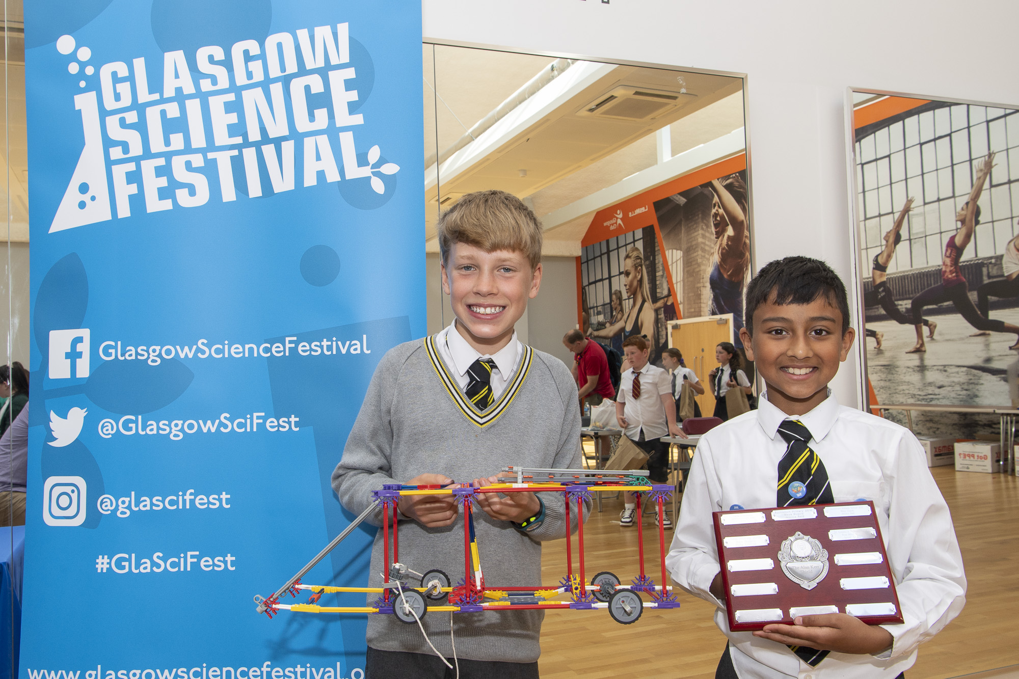 Photograph of the winning team, one is holding the model fire engine they built and the other is holding the Alan Kerr shield trophy. 