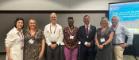 Attendees of the Academy of Management meeting 2023 standing for a group photograph beside a screen with slides. 